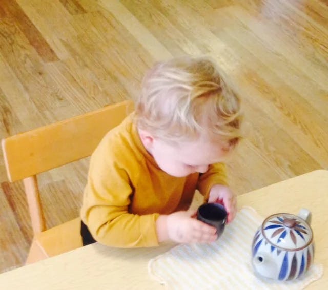 Child playing with a teapot and cup on a table