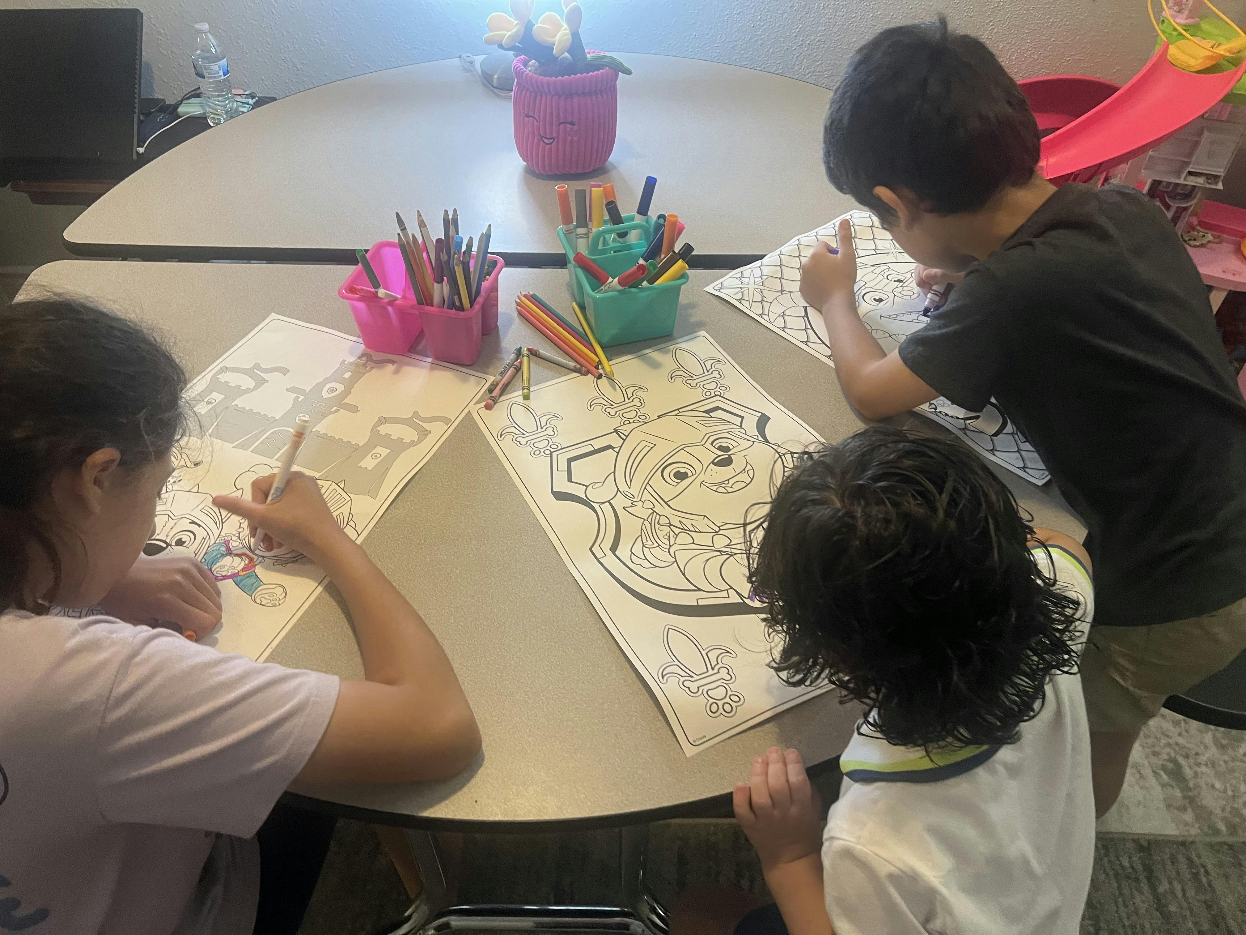 Three children coloring on sheets of paper at a round table