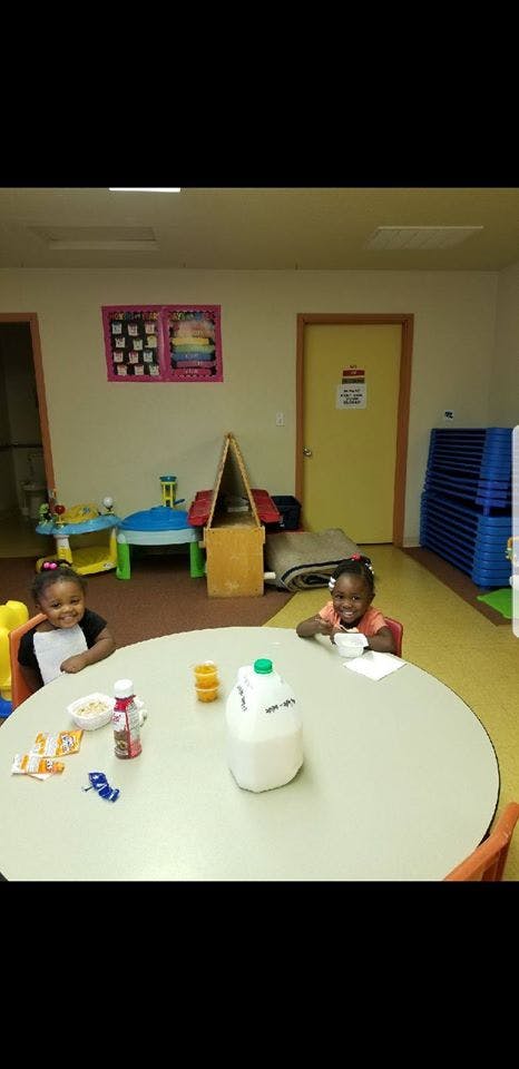 Two children sitting at a table with food and drinks