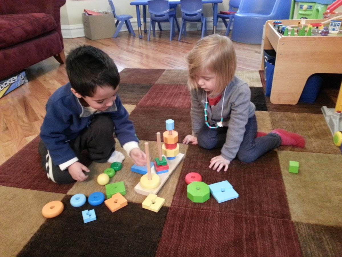 Two children playing with colorful blocks and stacking toys on a rug