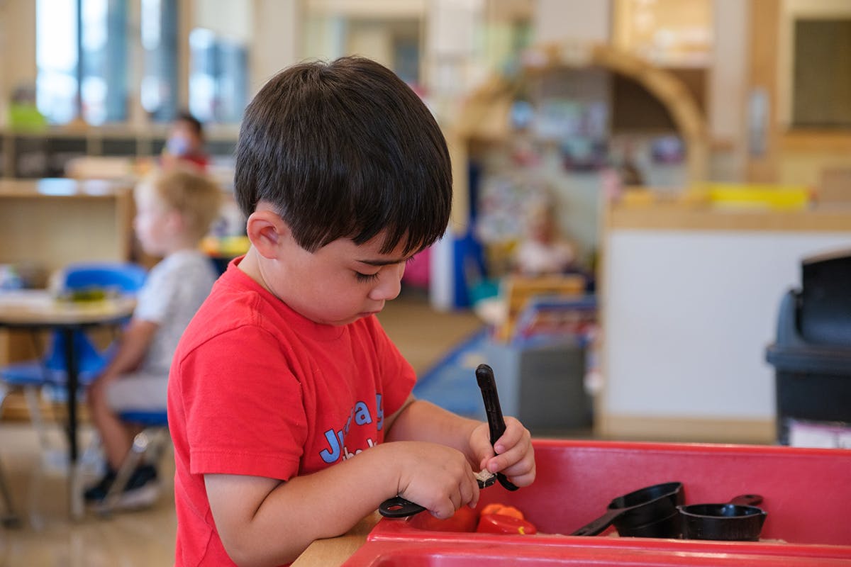 Child playing with objects in a red bin in a classroom