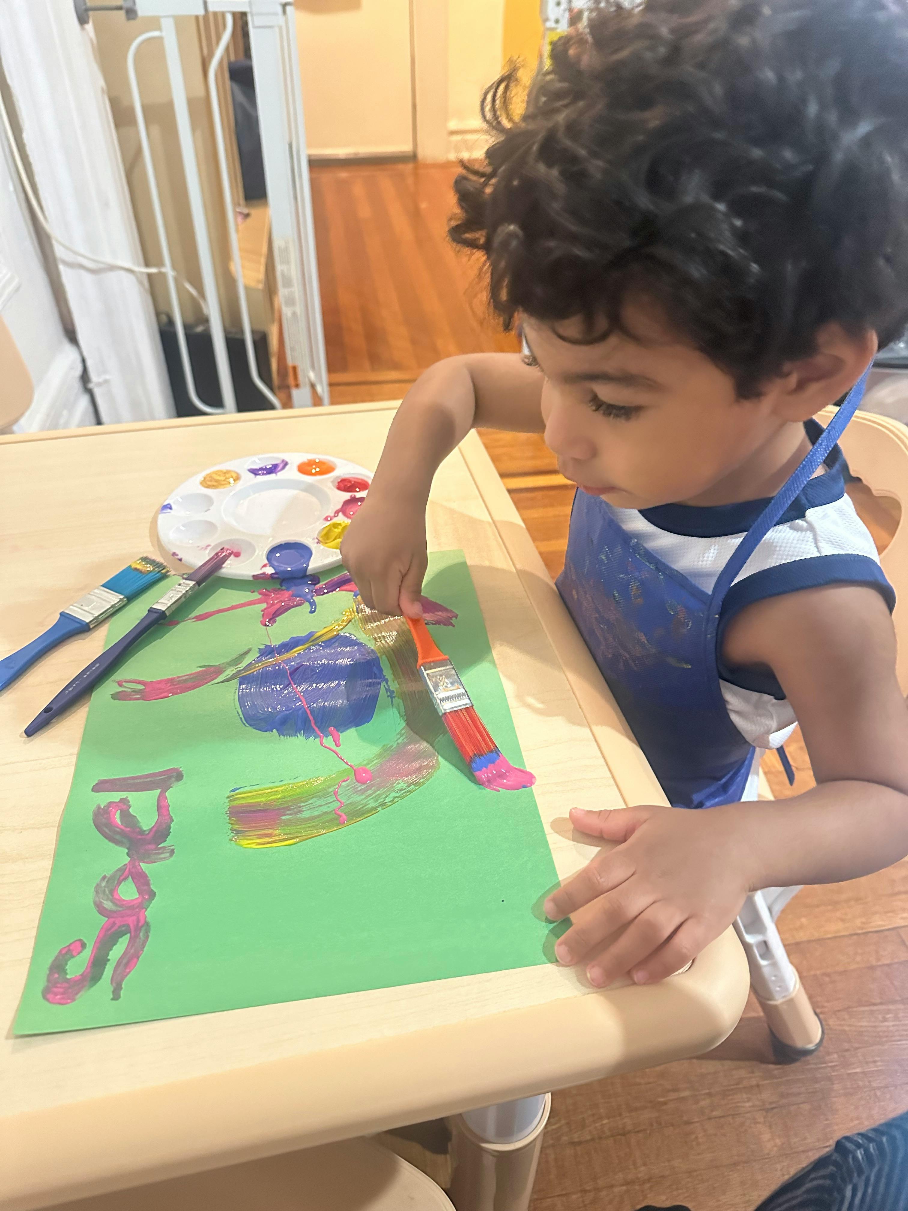 Child painting on green paper with a paintbrush
