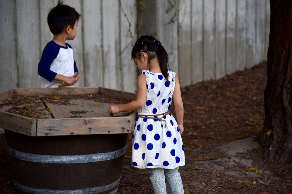 Two children looking into a wooden planter on top of a barrel