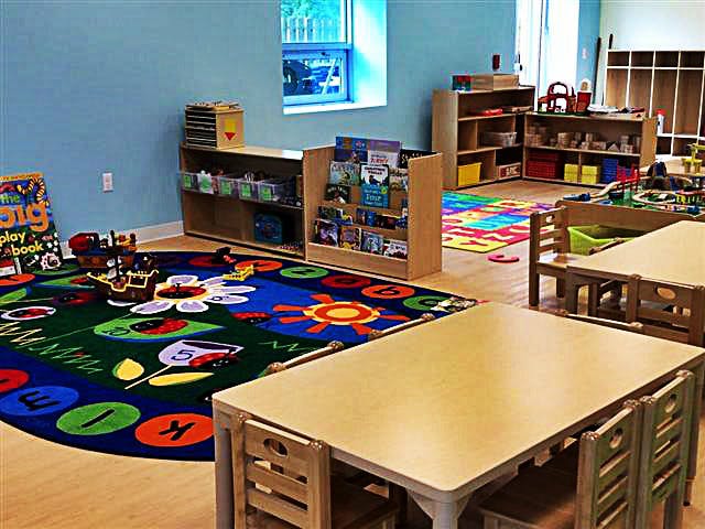 Classroom with small tables and chairs, colorful rug, and bookshelves