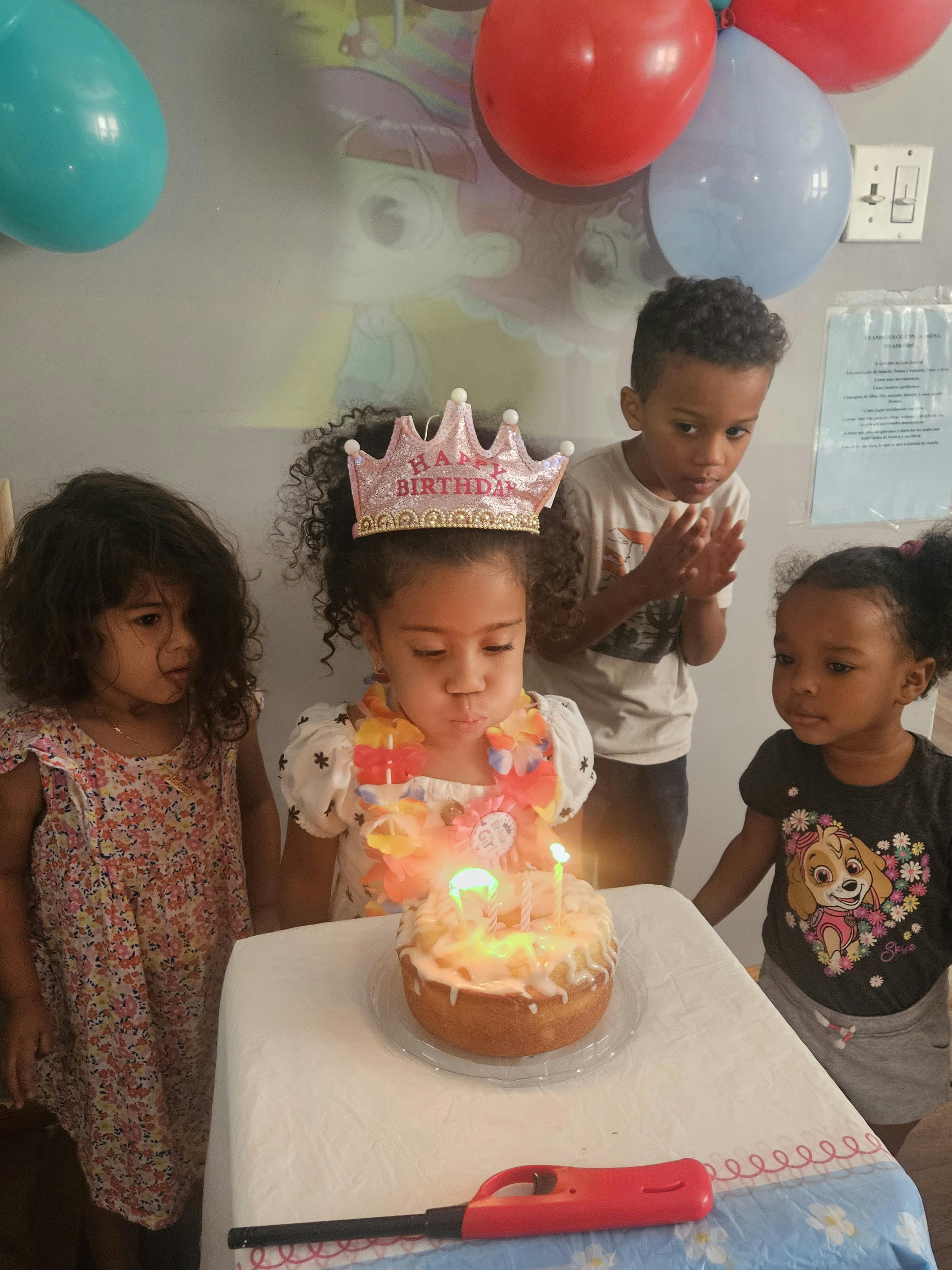 Child wearing a crown blowing out birthday candles as other children look on