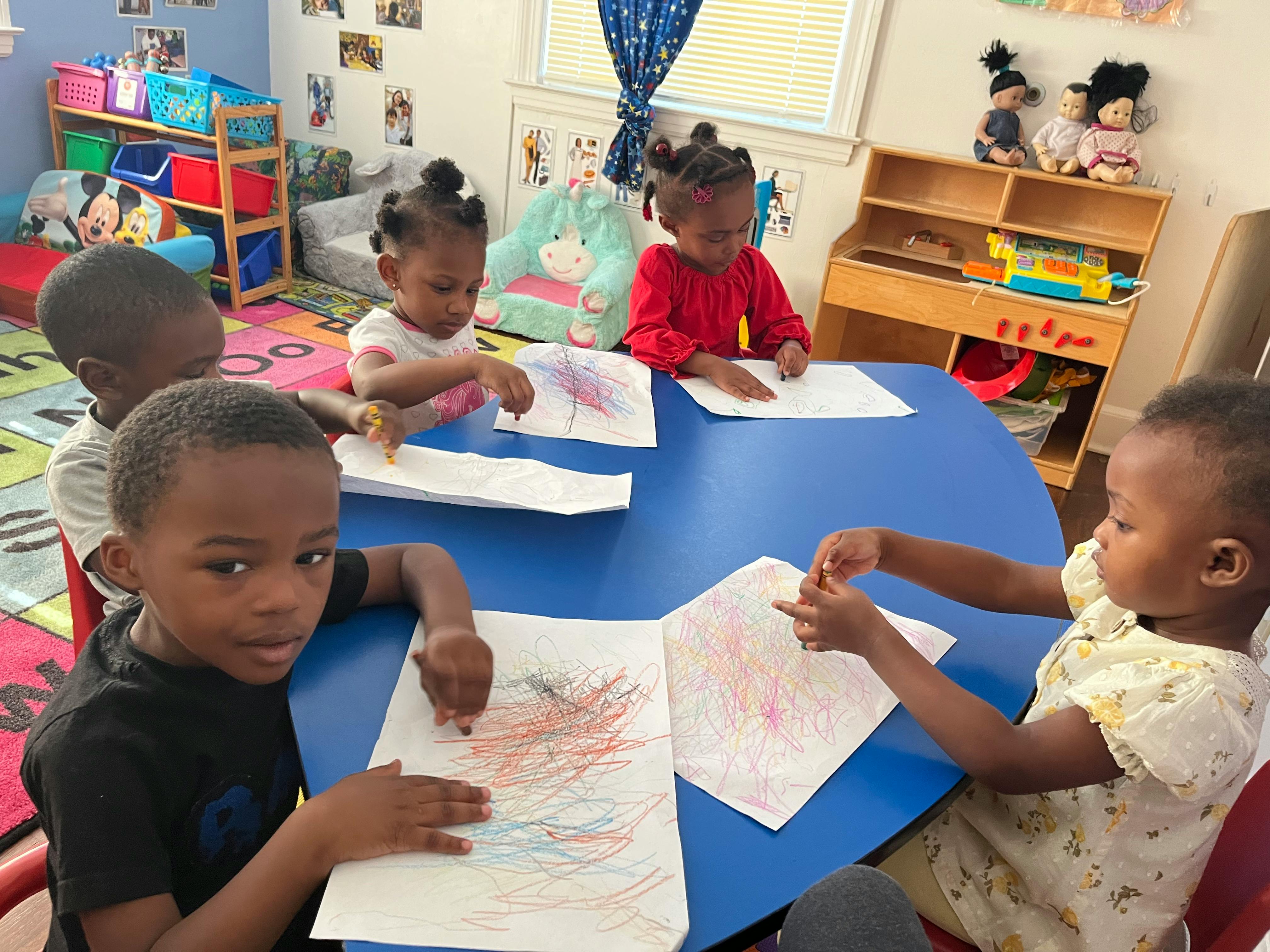 Children drawing at a blue table in a classroom