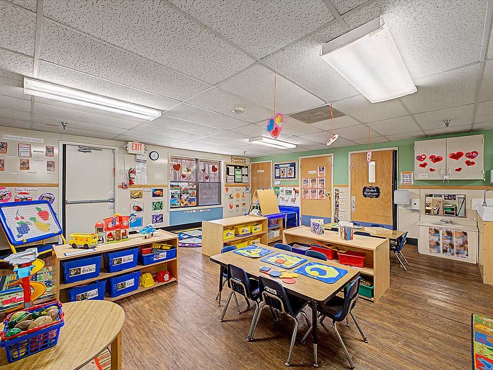 Empty classroom with small tables and chairs, shelves with toys