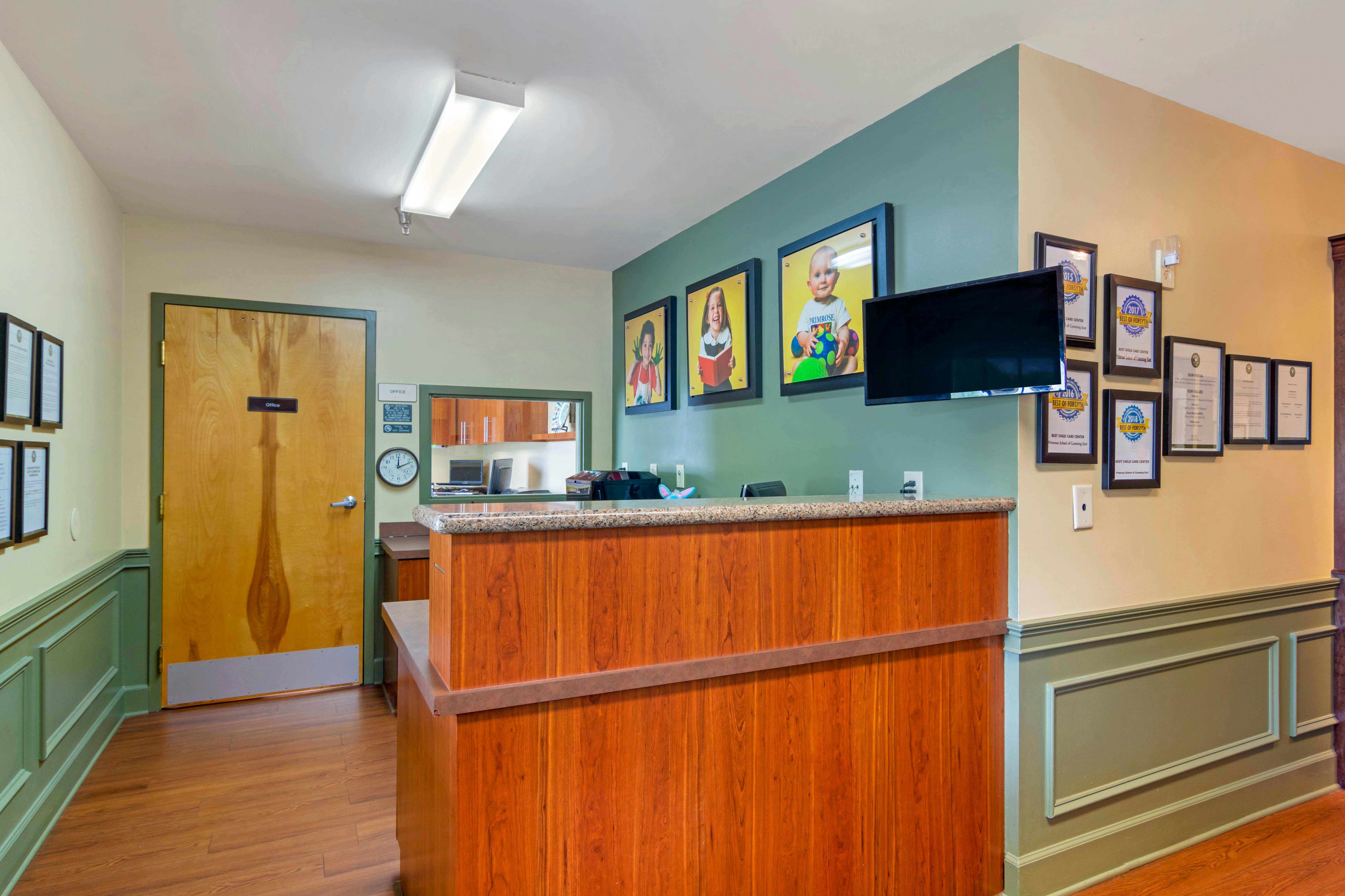 Reception area with a wooden counter, children's photos on a green wall, and framed certificates
