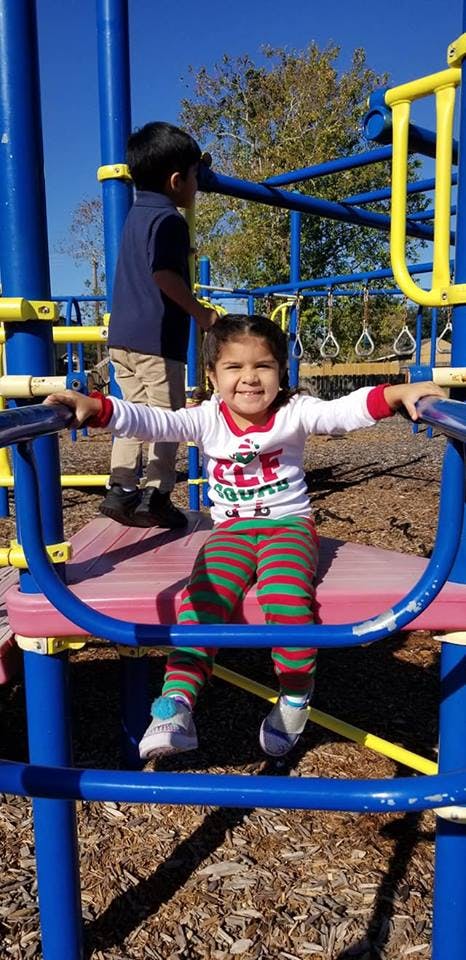 Child sitting on a playground structure with another child in the background