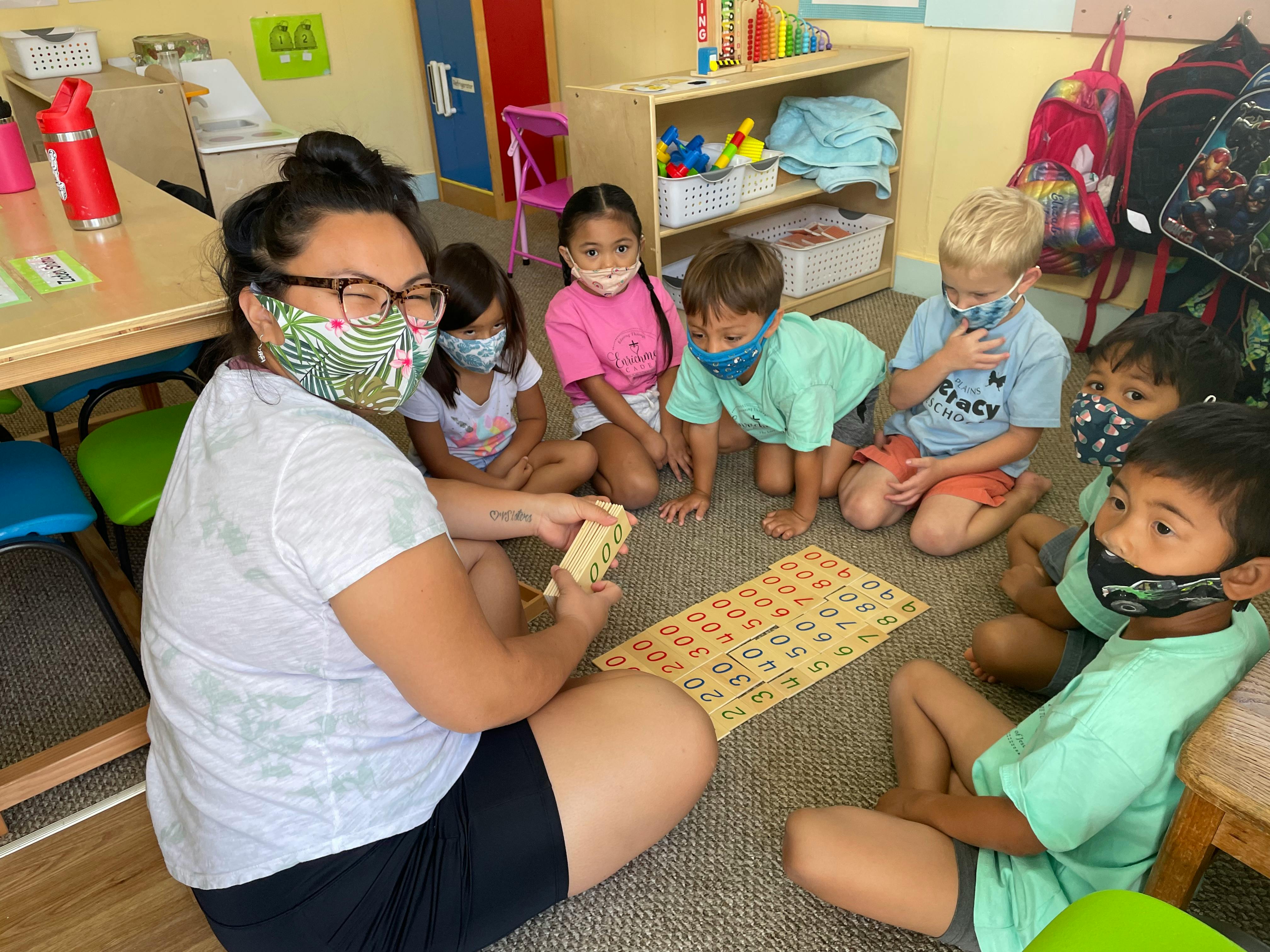 Person and children sitting on floor playing a game in a classroom