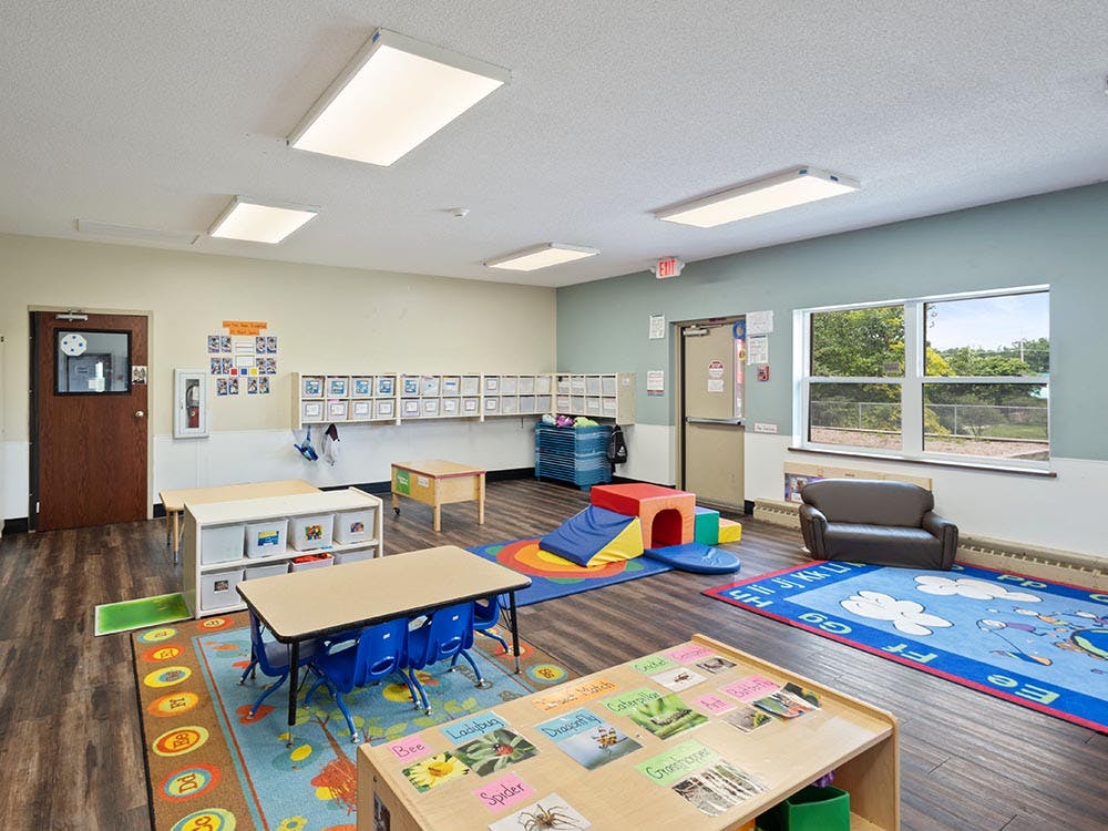 Empty colorful preschool classroom with small tables, chairs, and play equipment
