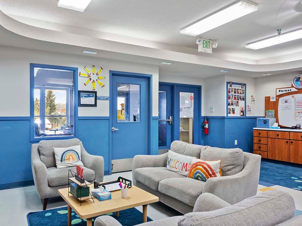 Lounge area in a classroom with gray couches, blue walls, and a wood table