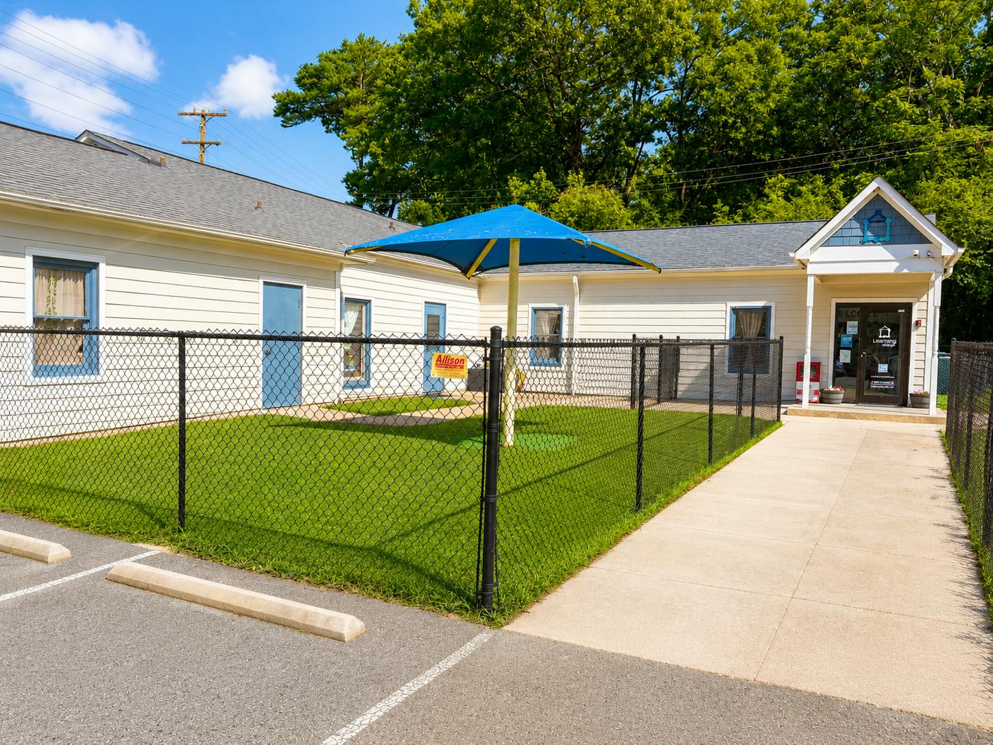 Childcare facility exterior with a fenced grassy play area and blue shade canopy