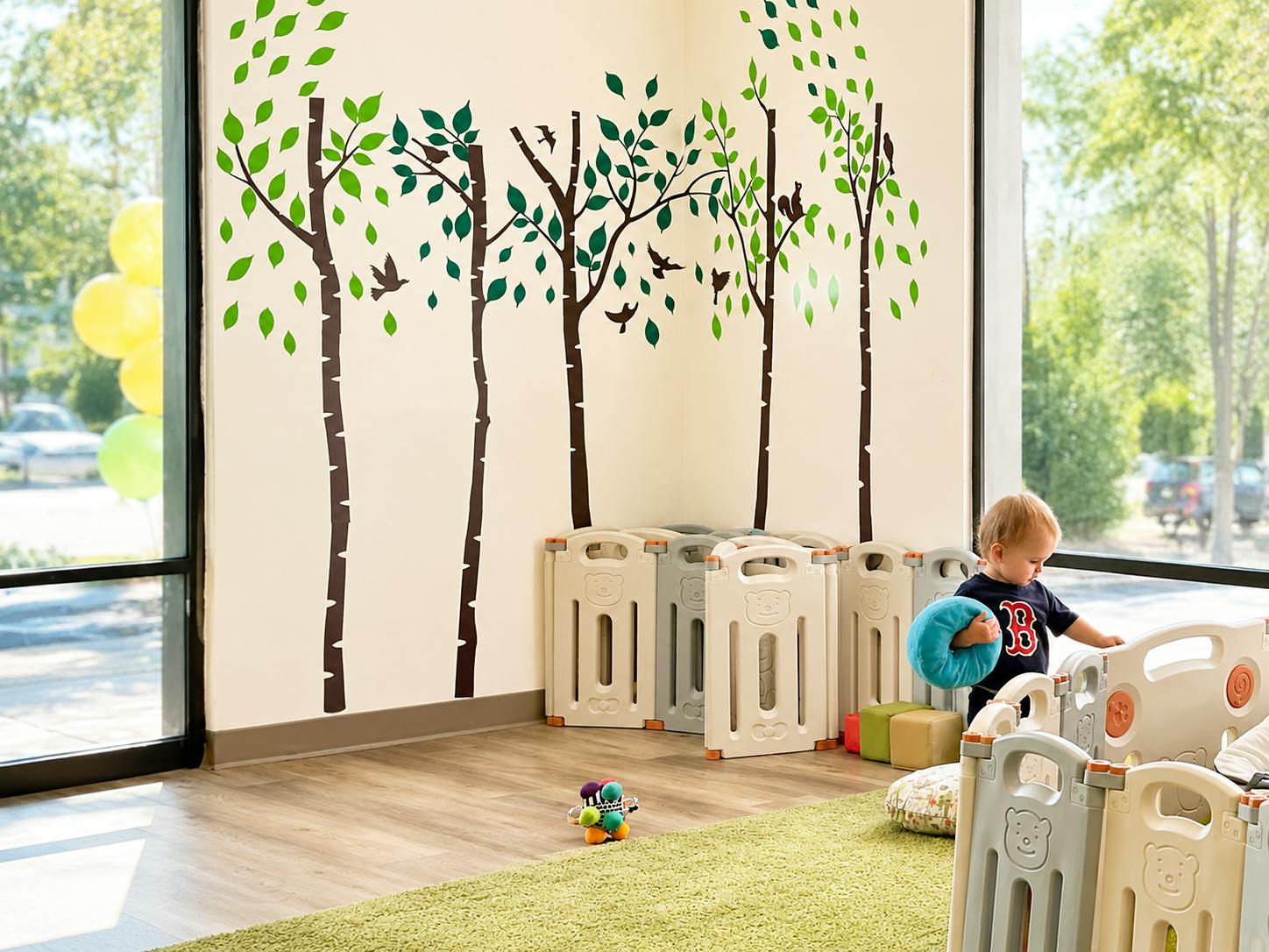 A child playing with a toy in a room with tree wall decals and playpen panels