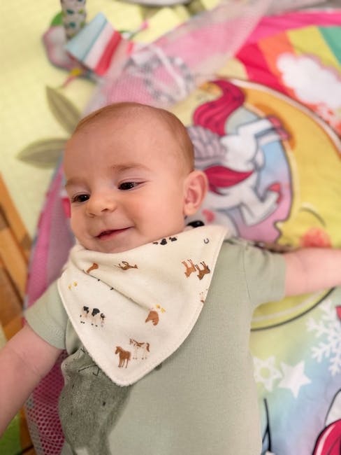 Baby wearing a printed bib lying on an activity mat