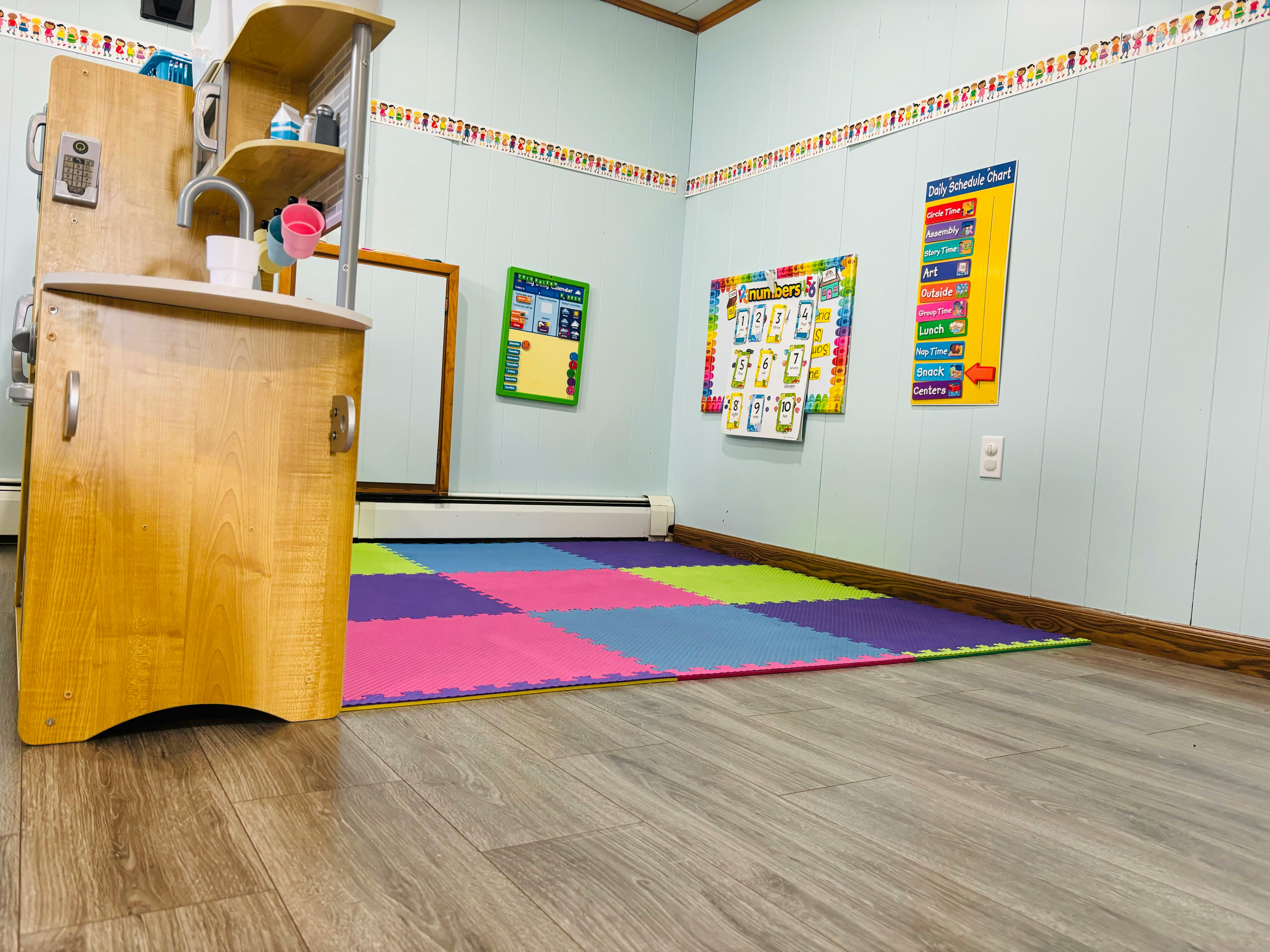 Play kitchen in a room with colorful floor mats and posters on the wall