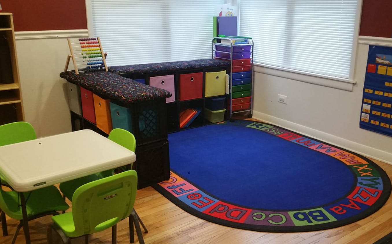 Classroom with small table and chairs, storage unit, and alphabet rug