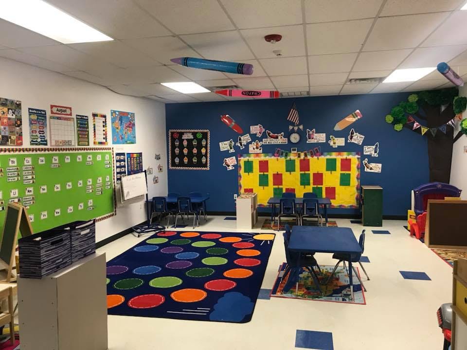 Empty classroom with colorful rug, small tables, and decorations on walls