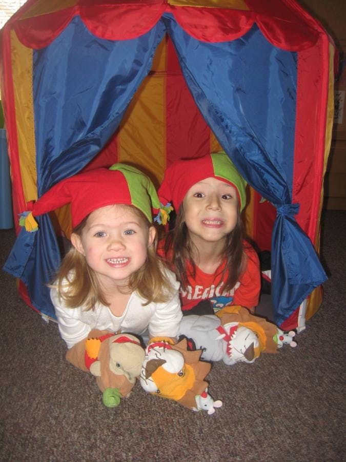 Two children wearing jester hats in a play tent with stuffed animals