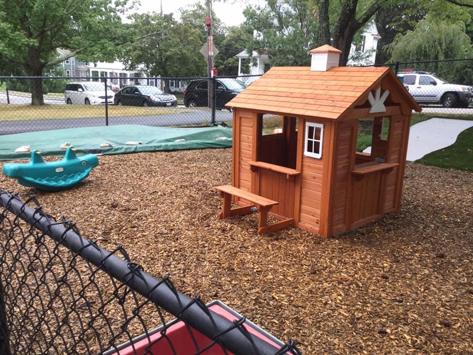 Wooden playhouse and a blue seesaw on a playground with wood chips