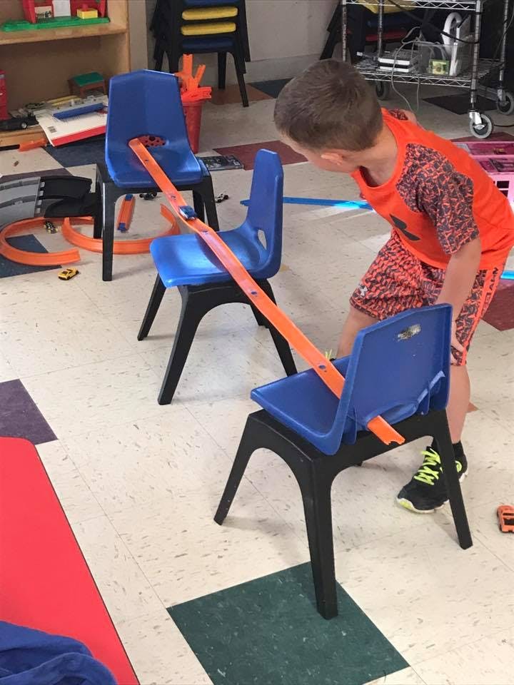 Child playing with a toy car track set up on chairs