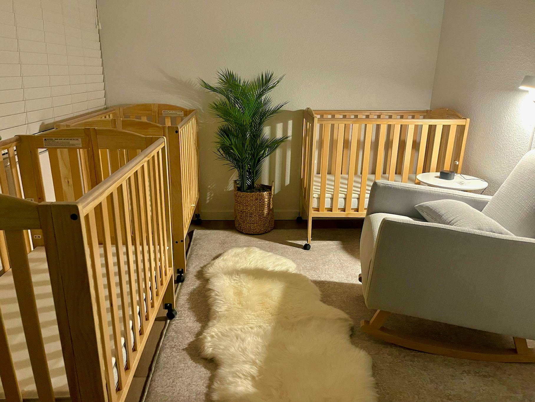 Two wooden cribs, a plant, and a rocking chair in a room