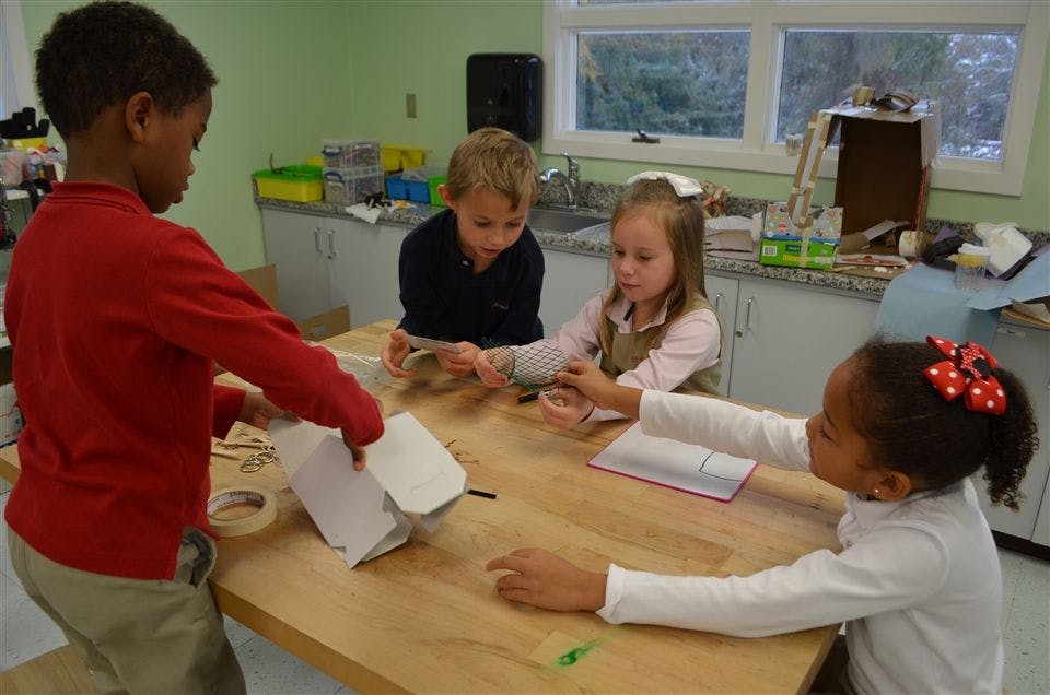 Four children working on crafts at a table in a classroom