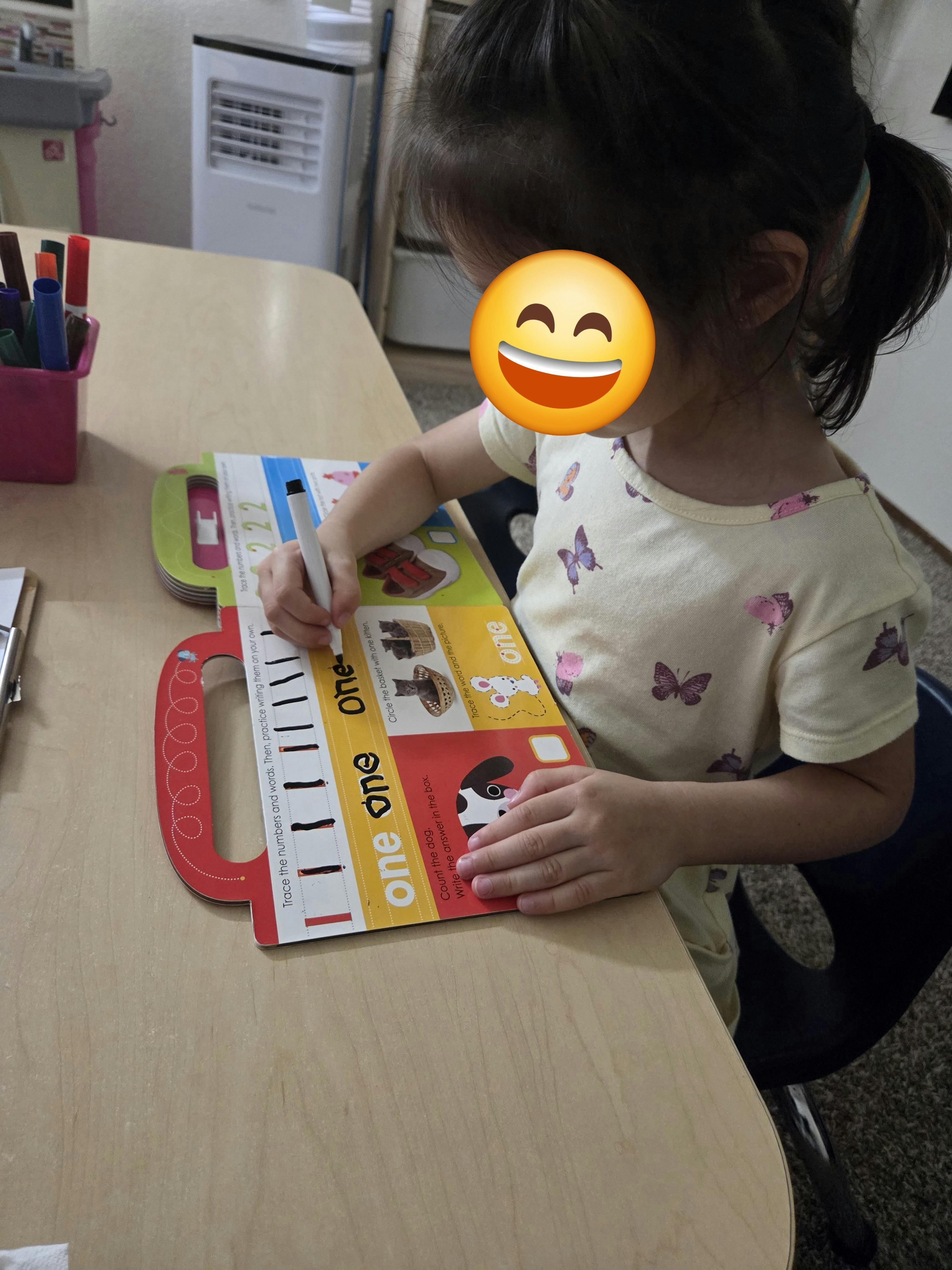 child tracing words in a workbook with a marker at a table