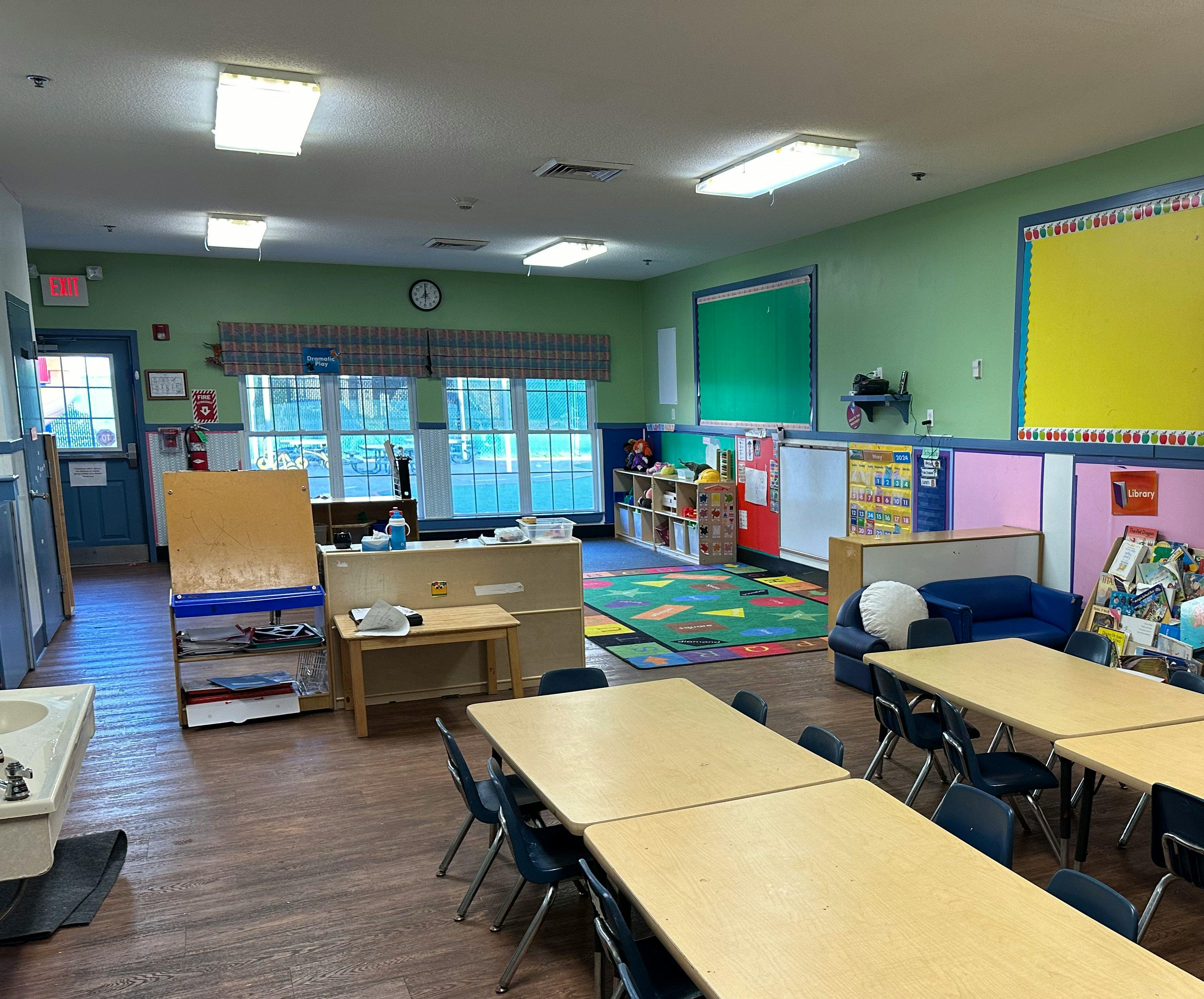 An empty classroom with light green walls and small tables and chairs