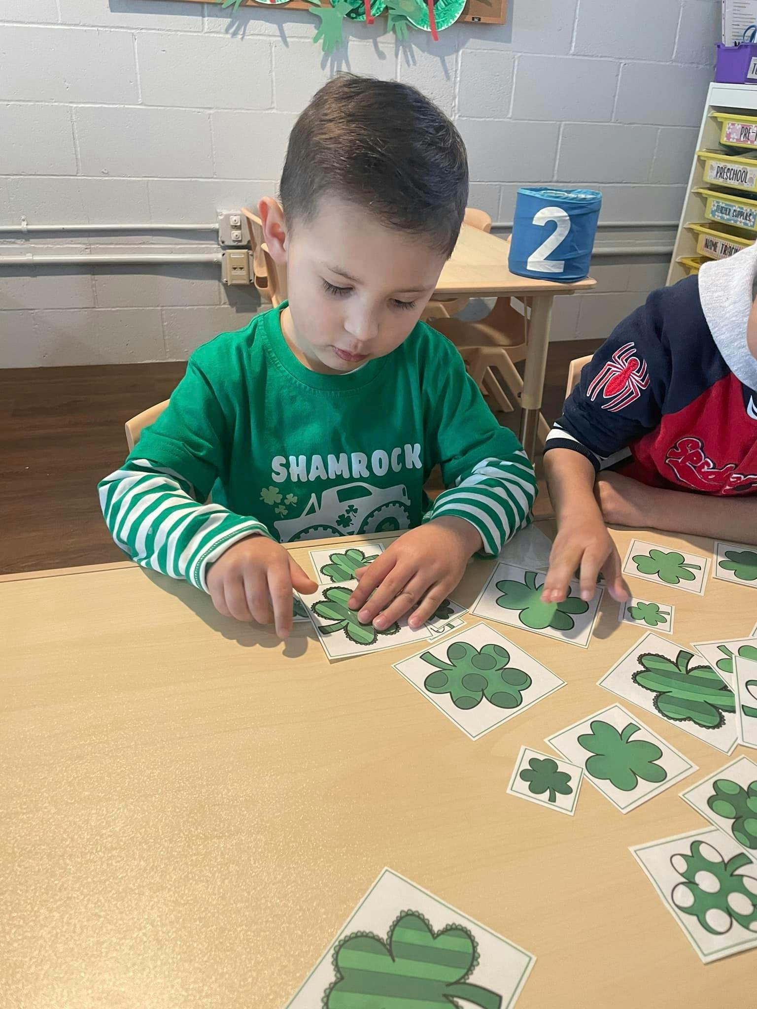 Child in green shirt playing with shamrock cutouts at a table
