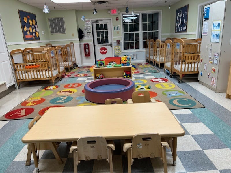 Cribs and small tables in a childcare room with an alphabet rug