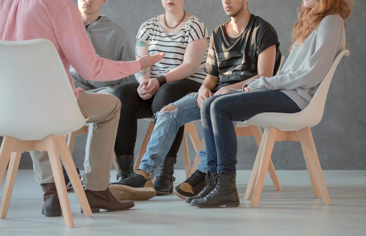 Group of people seated in a circle, one person speaking with a gesturing hand