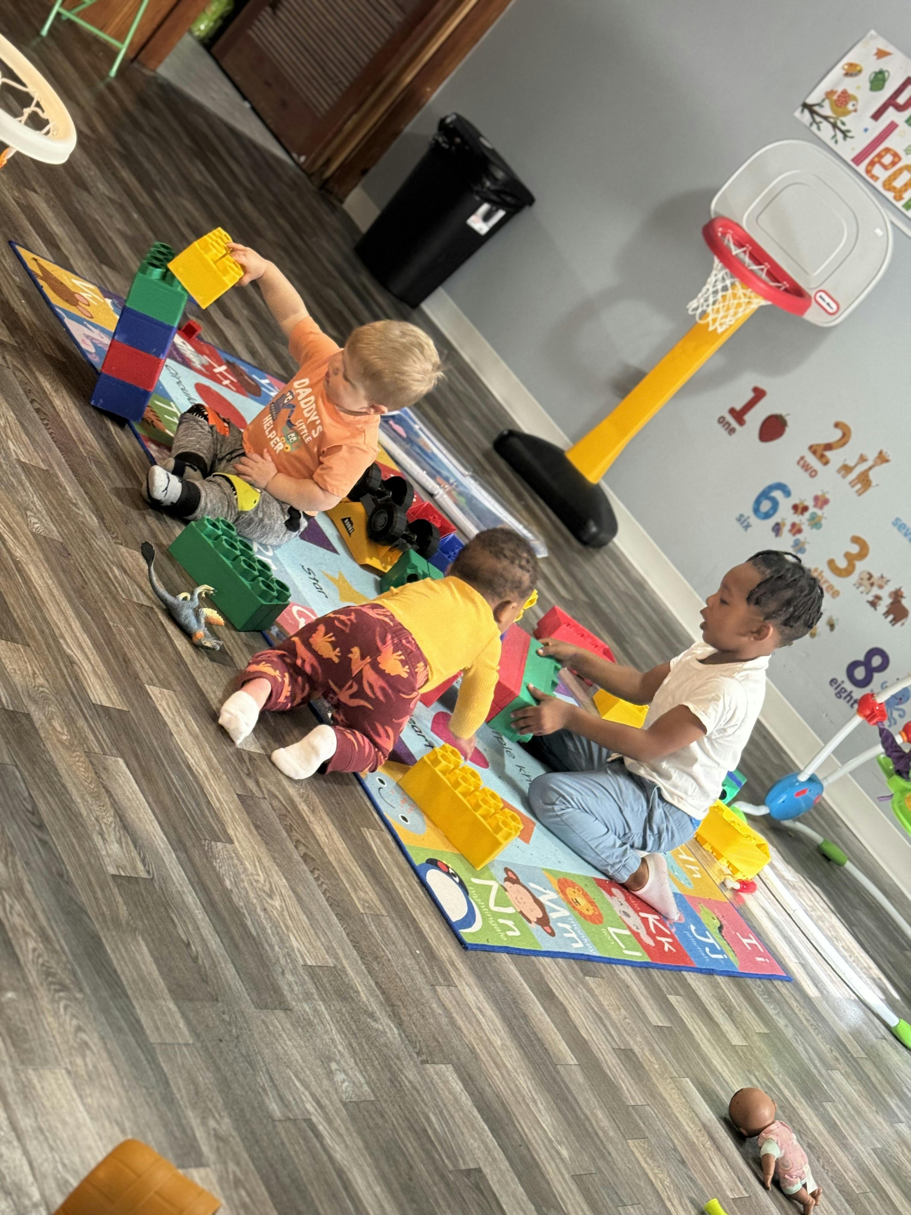 Three children playing with building blocks on a mat
