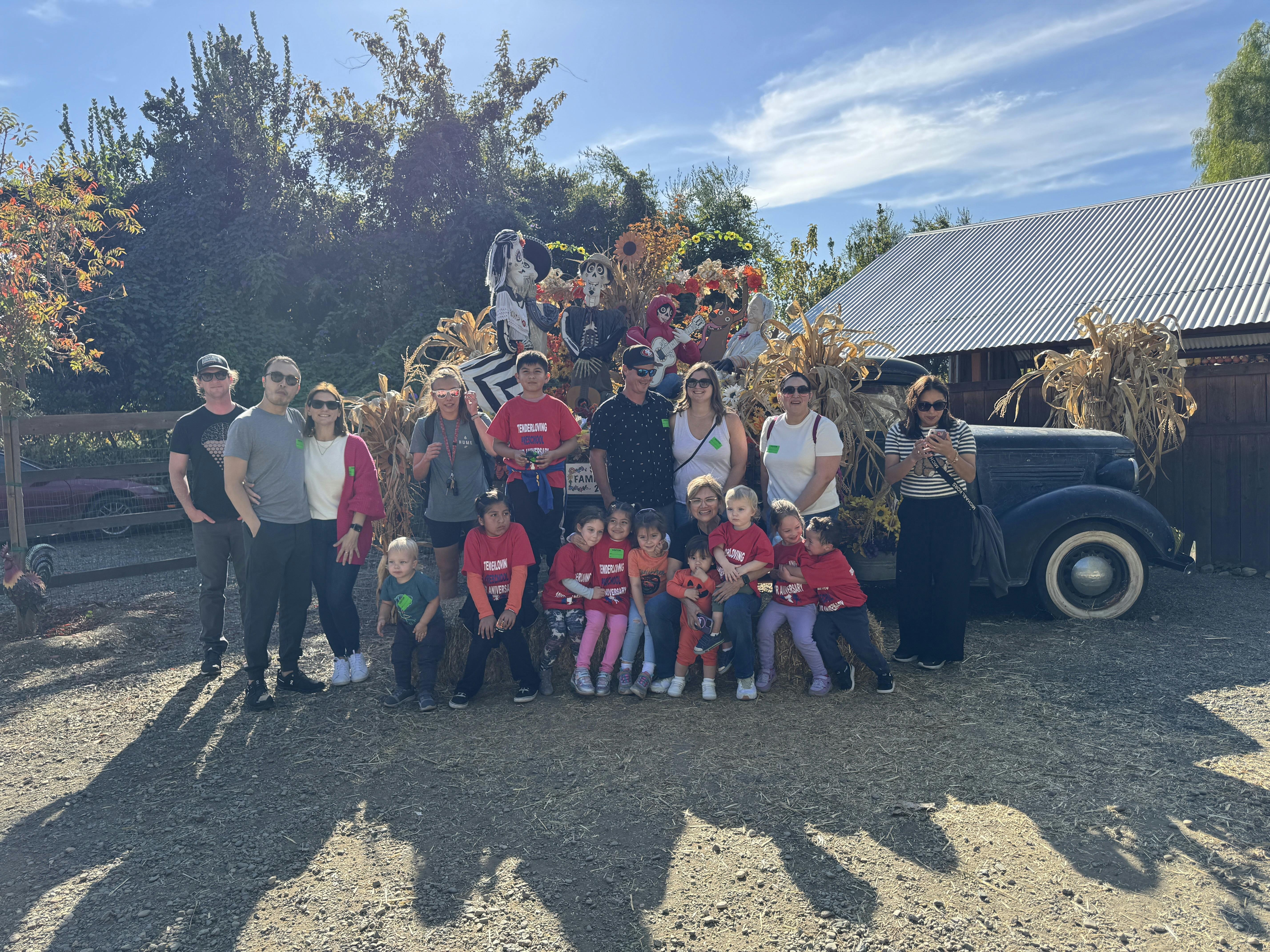 Group of adults and children posing outdoors with an old car and fall decorations