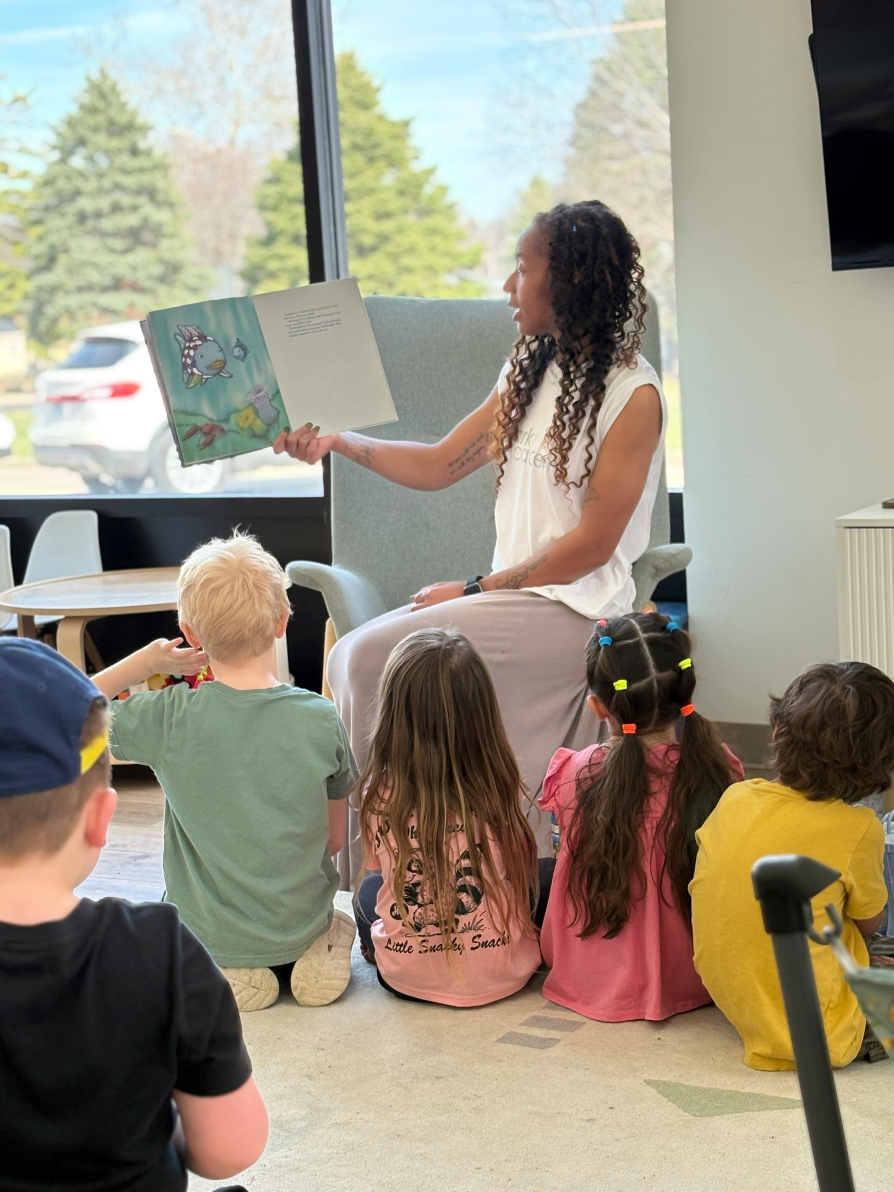 A person reading a book to several children sitting on the floor in a classroom