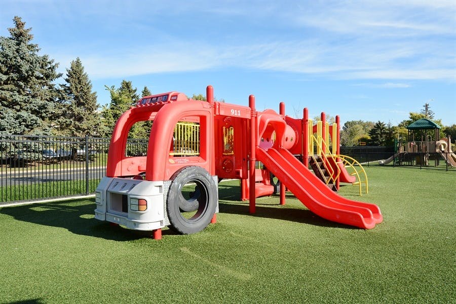 Red fire truck shaped playground equipment with a slide on artificial turf
