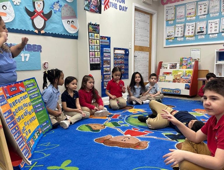 Children sitting on a rug in a classroom with an adult nearby