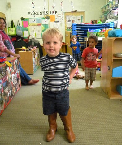 Child in striped shirt and boots standing in a classroom