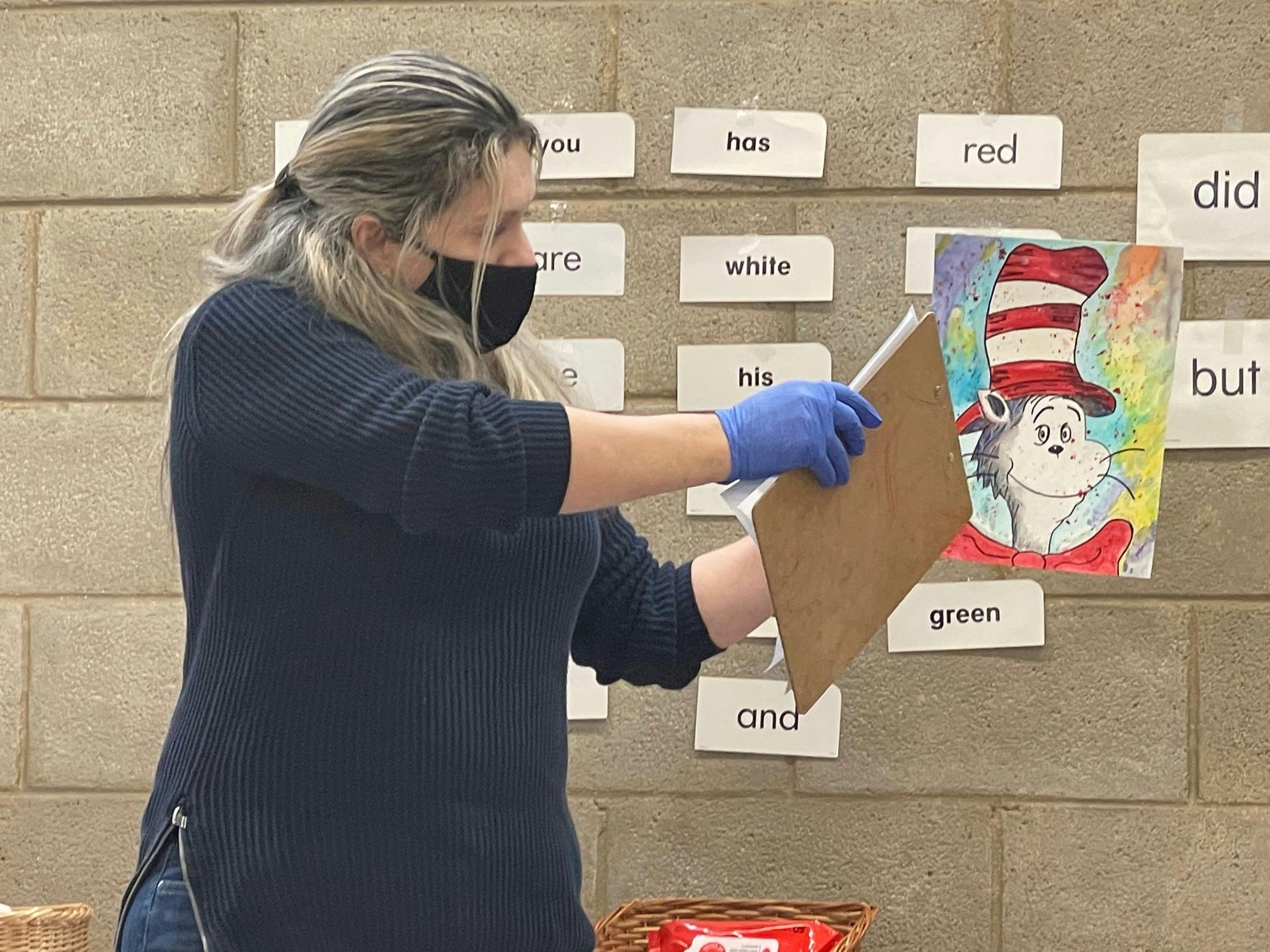 Person in mask and gloves holding a clipboard in front of a wall with word cards
