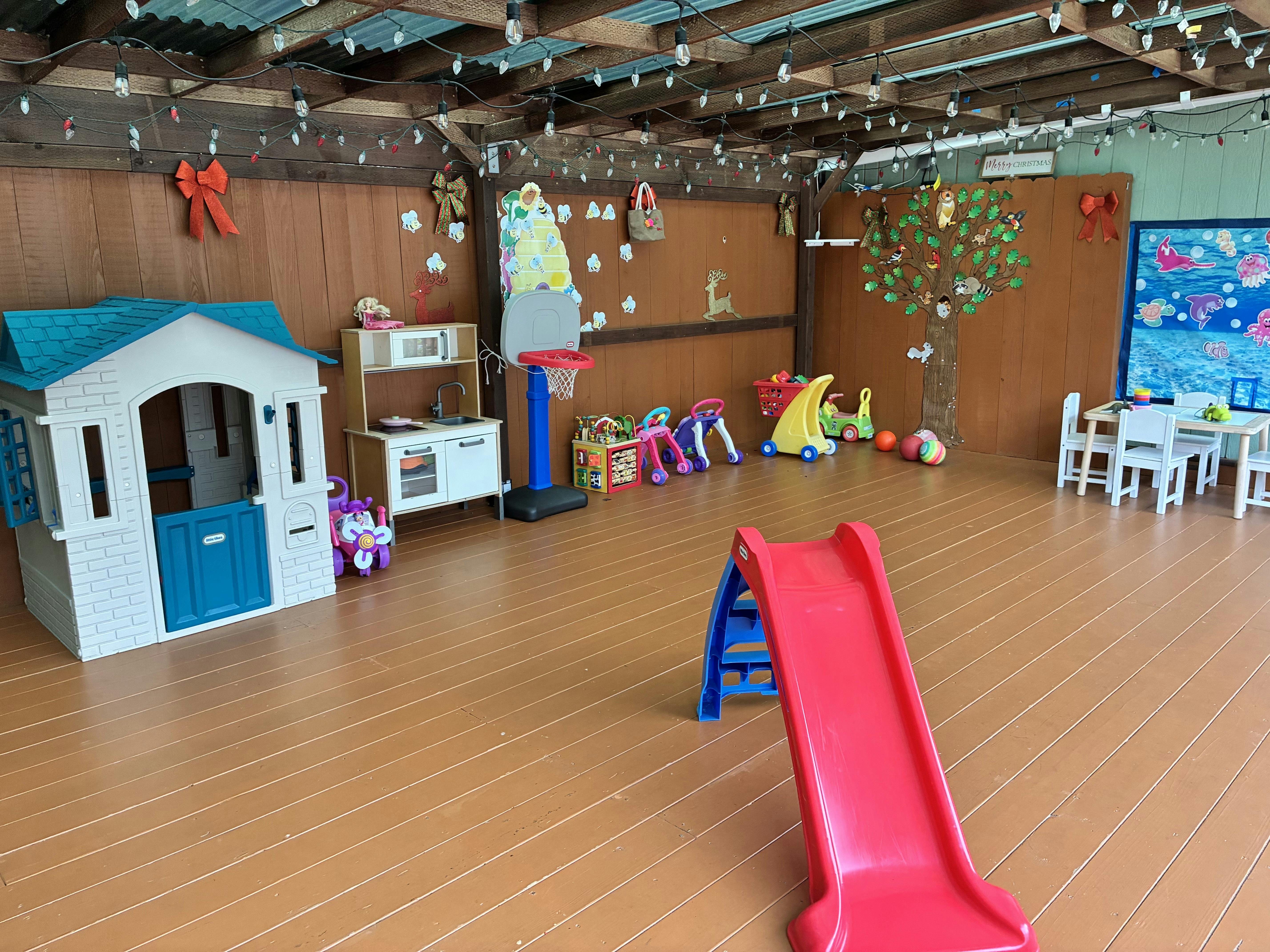 Covered outdoor play area with a toy house, slide, and various children's toys