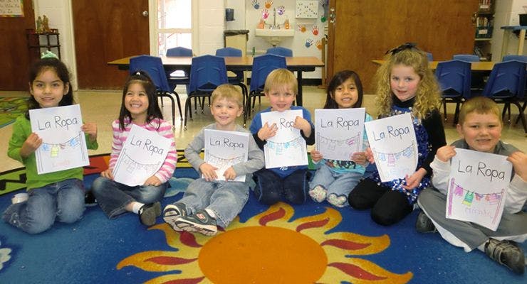 Children sitting on a rug holding up papers with text
