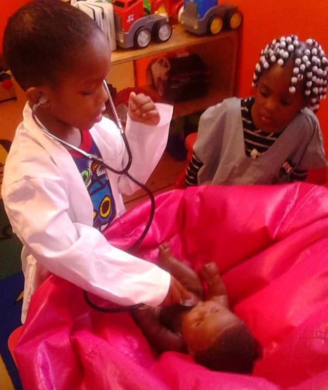 Child in doctor's coat using a stethoscope on a baby doll