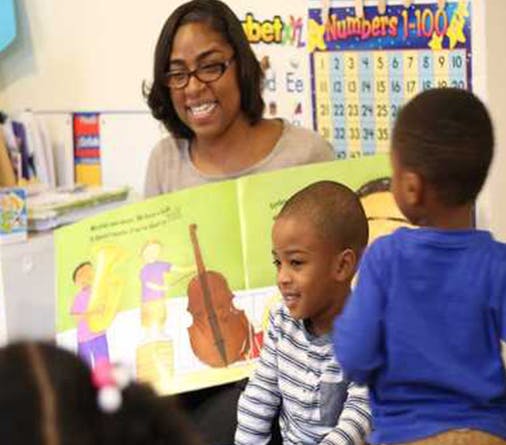 Person reading a book to two children in a classroom