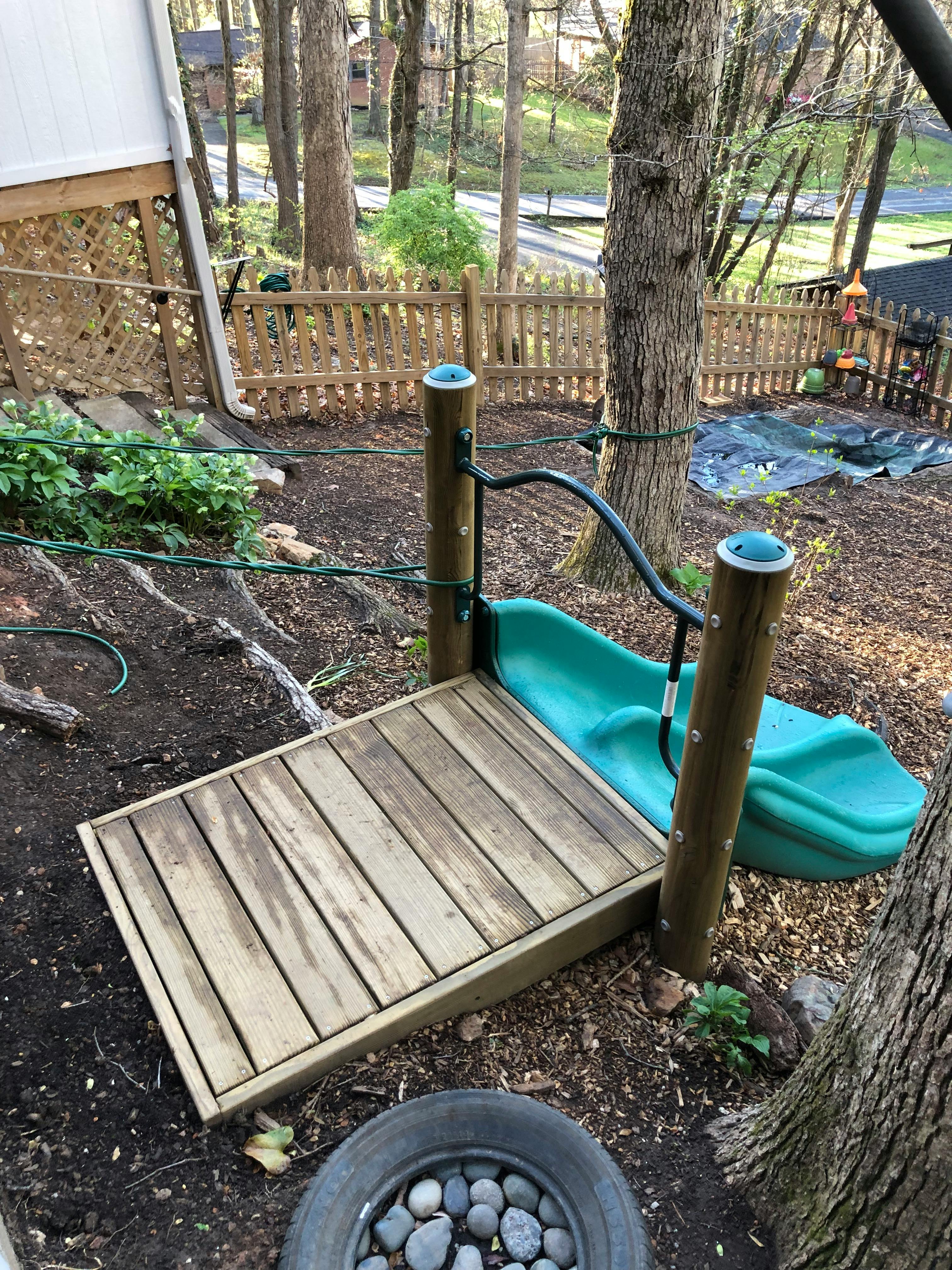 Wooden platform with a green slide and black handrail attached to a tree