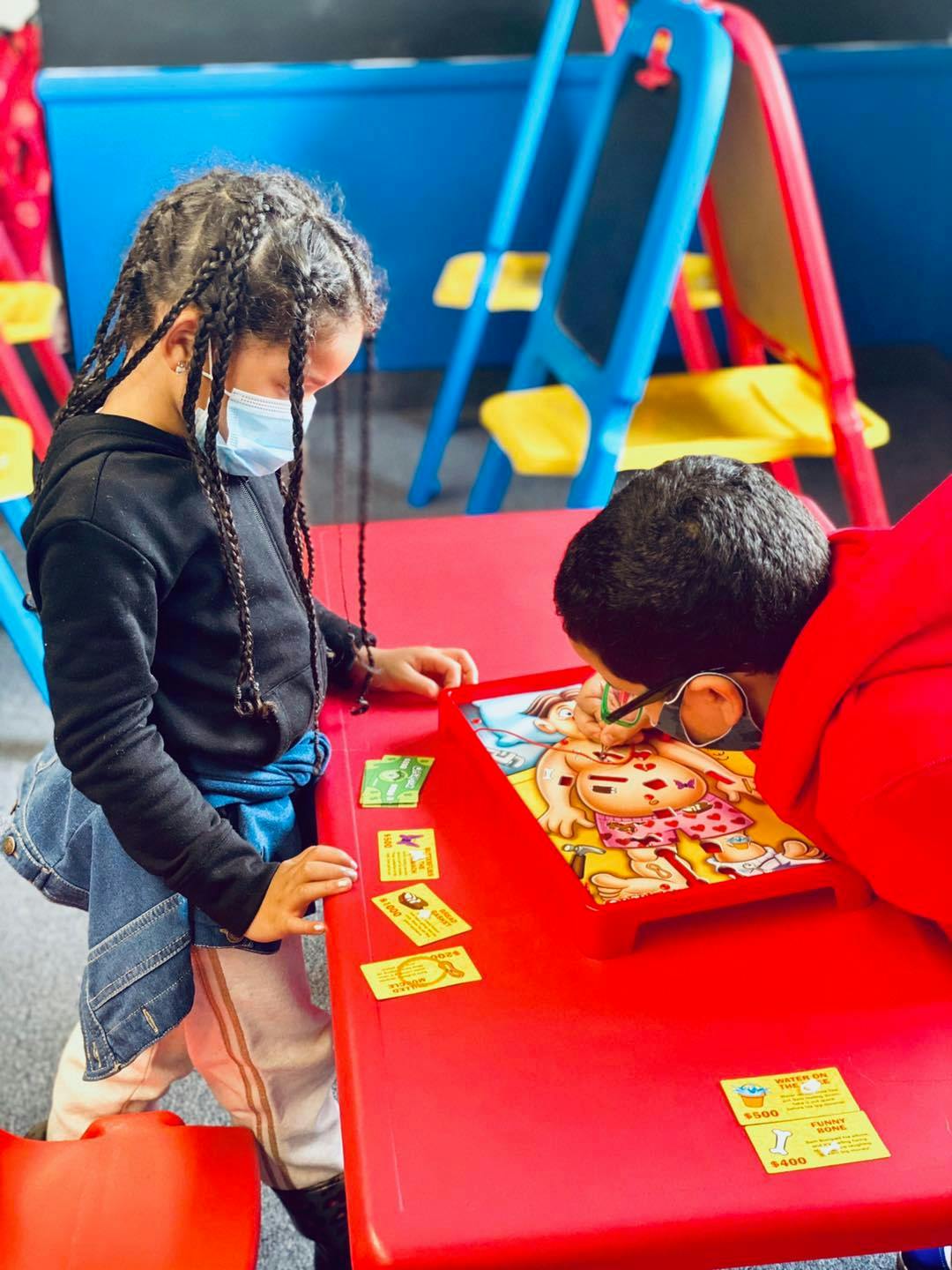 Two children playing a board game at a red table