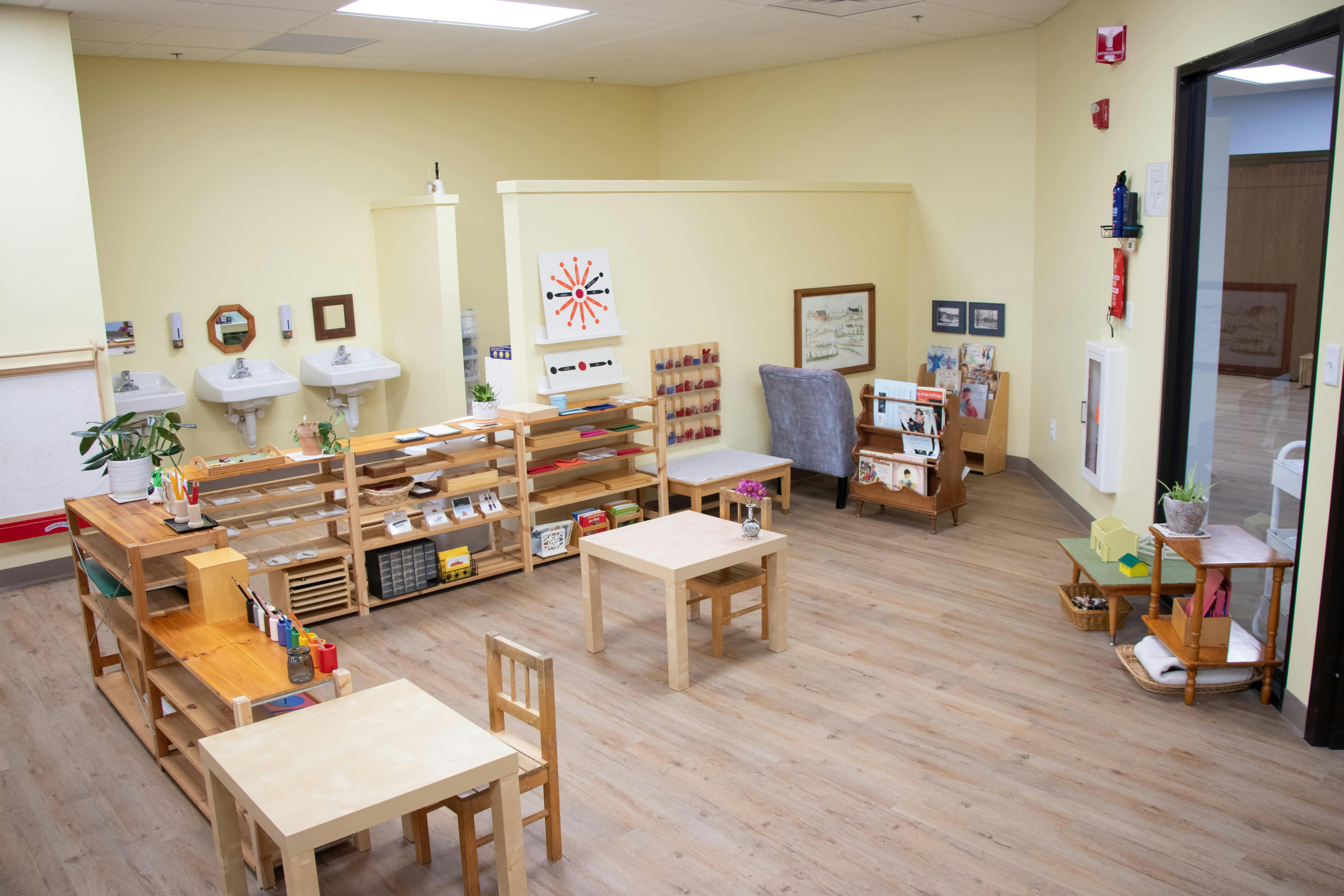Classroom with small tables and chairs, shelves with learning materials, and sinks