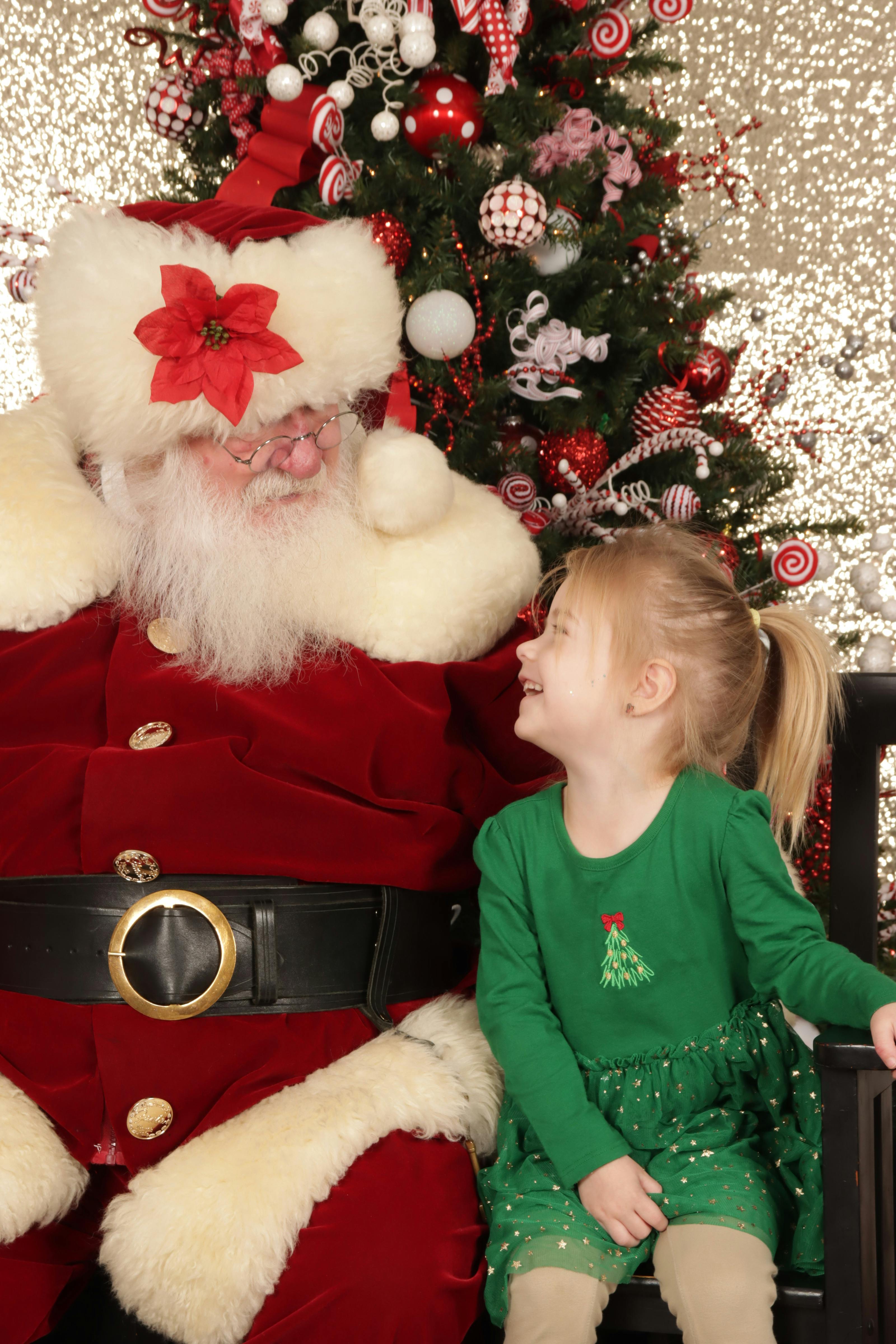 Santa Claus in red coat, black belt, and white beard with a child in green dress
