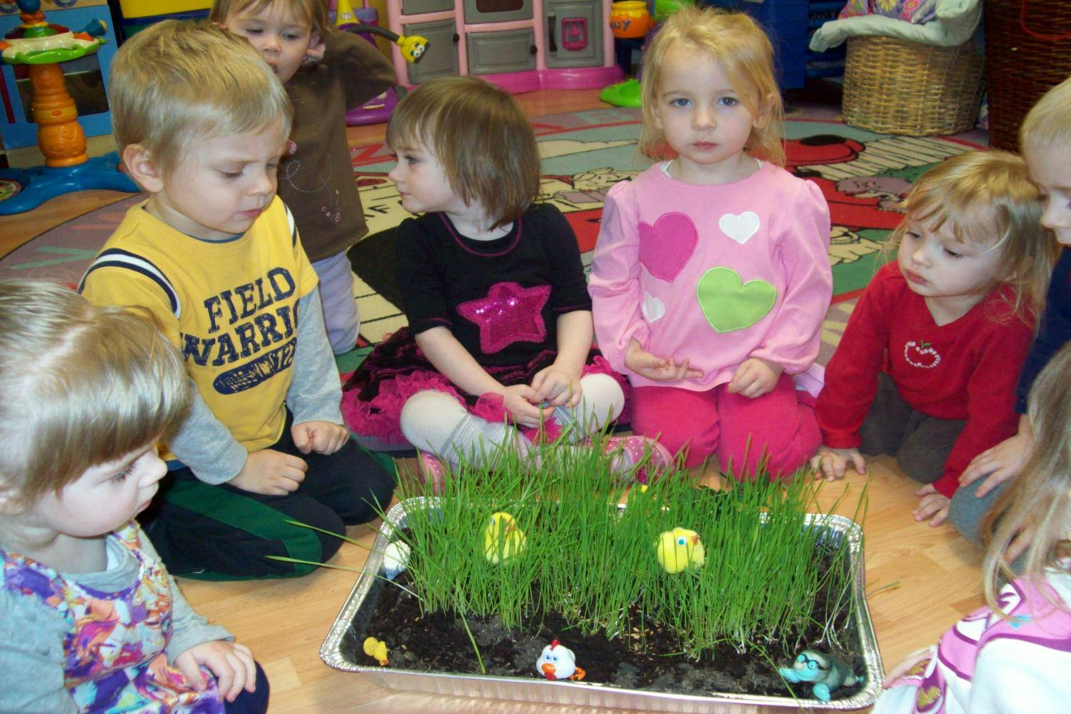 Children sitting around a tray of grass with small decorations