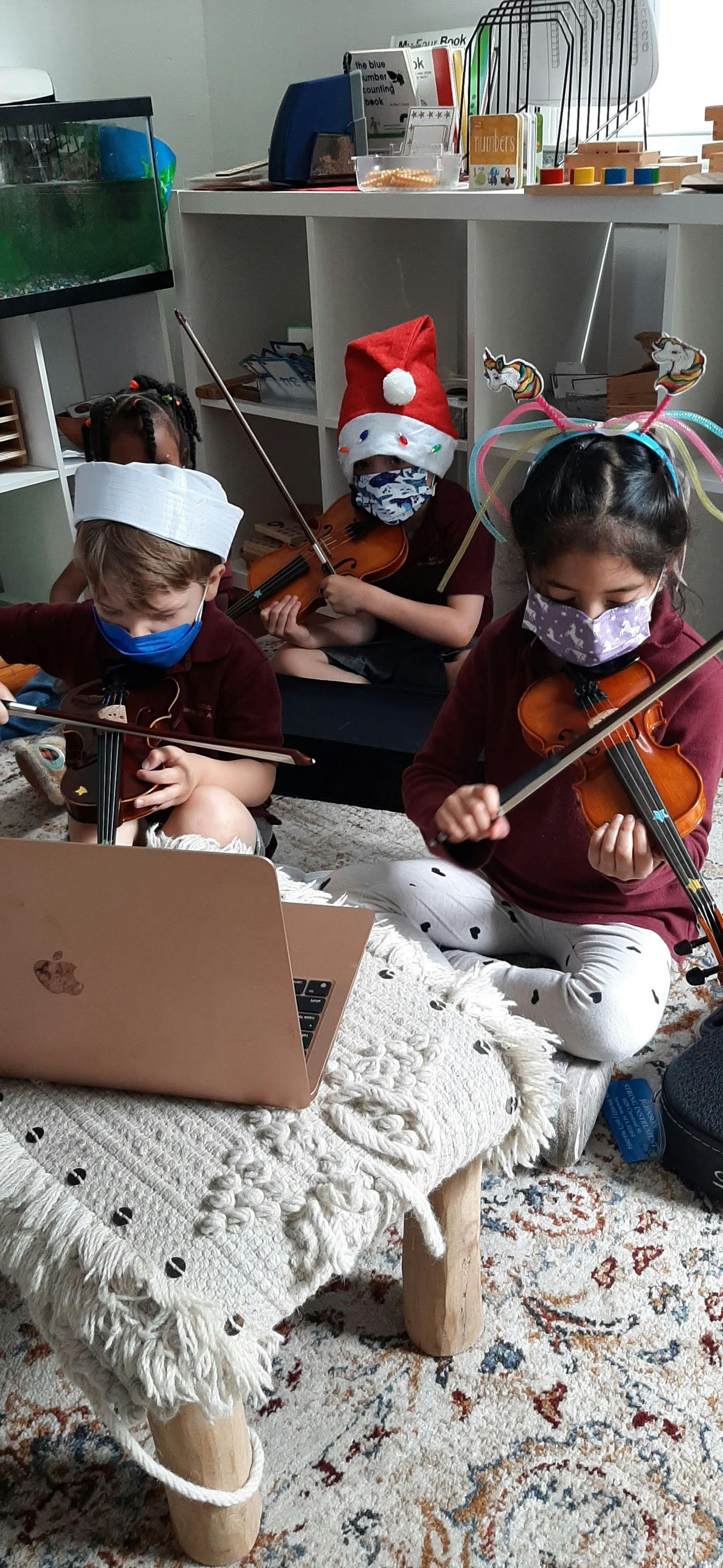 Children in masks playing violins with a laptop nearby