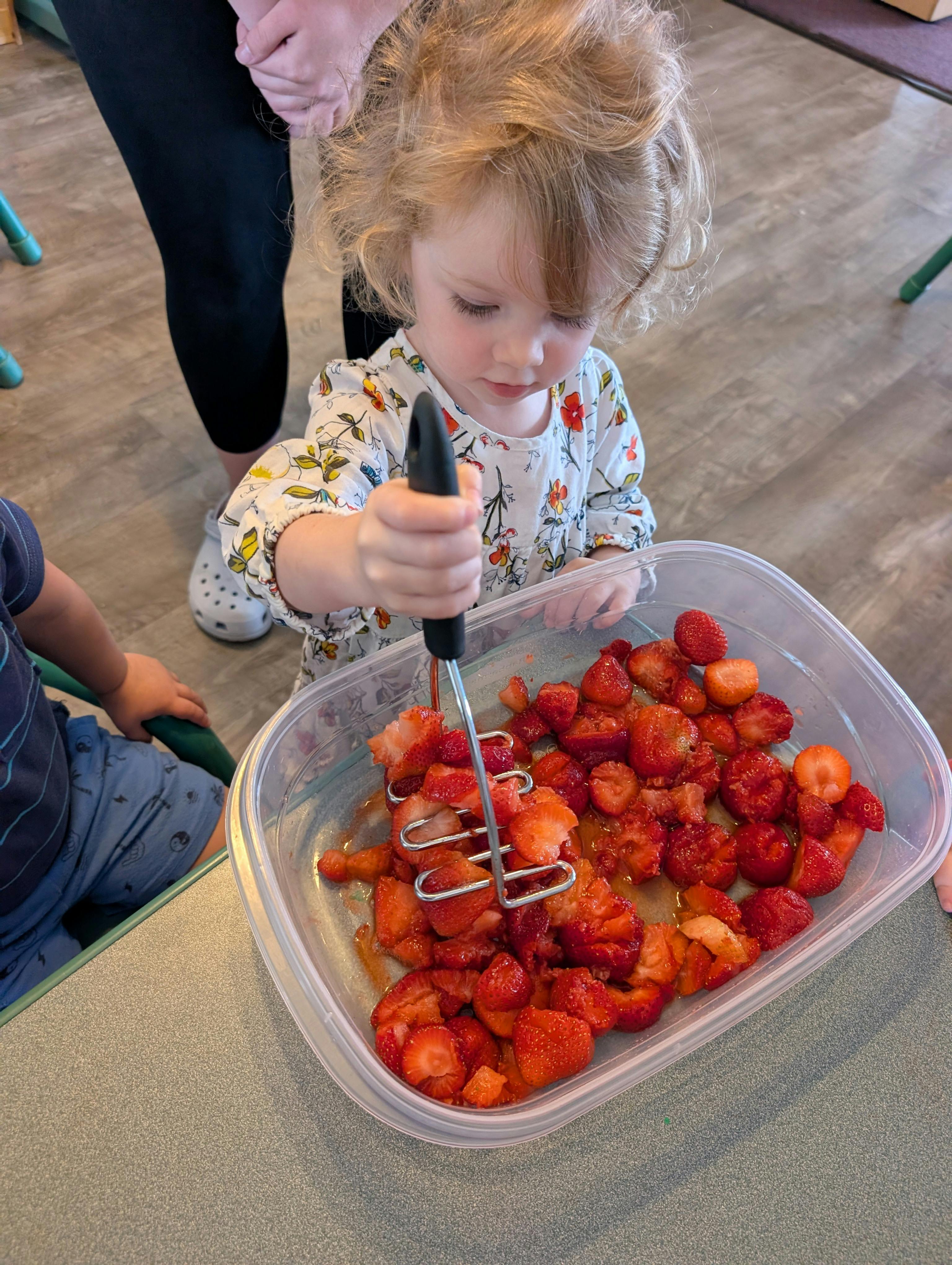 Child mashing strawberries in a container